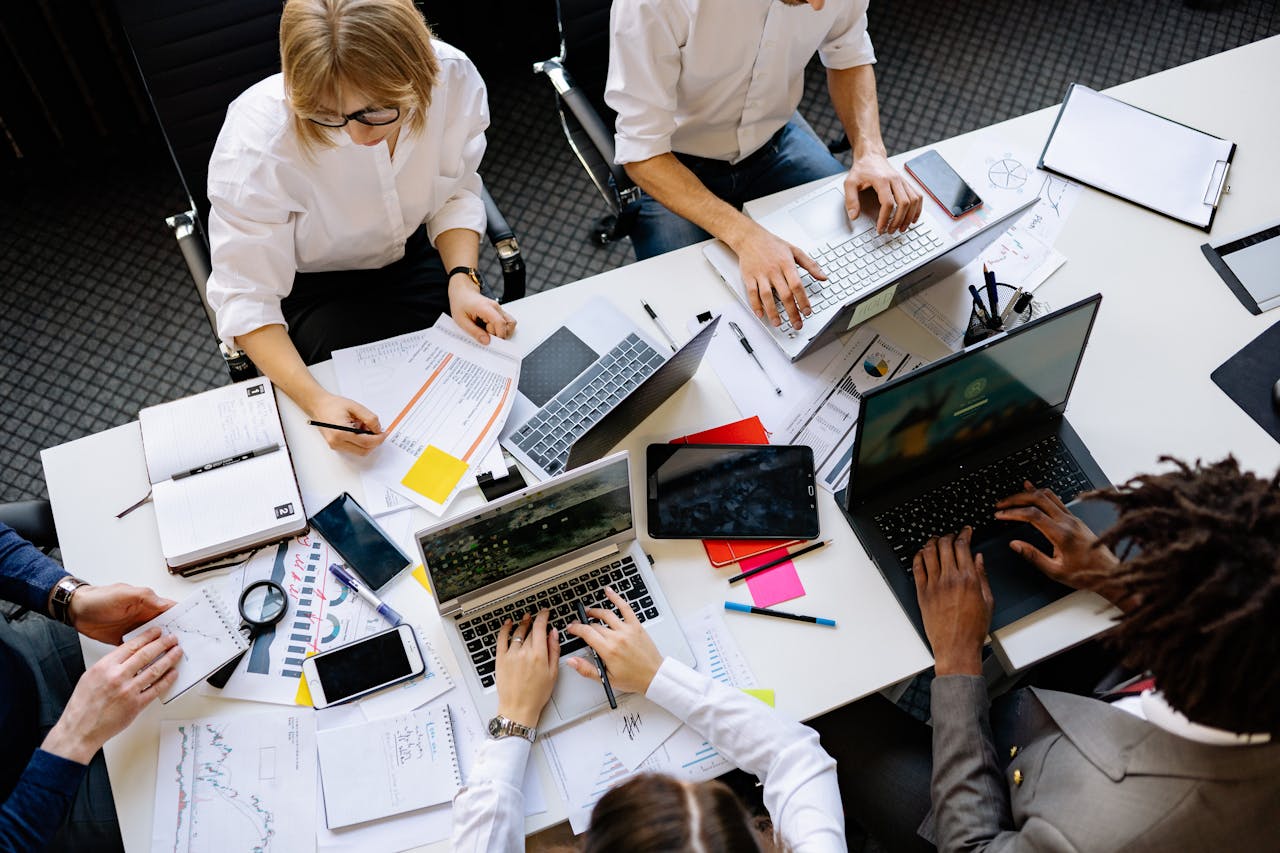 Vibrant office teamwork scene with laptops, documents, and diverse professionals in a meeting.